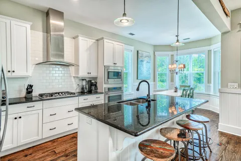 a kitchen with stainless steel appliances granite countertop a stove a sink dishwasher and white cabinets with wooden floor