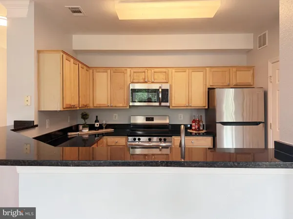 a kitchen with stainless steel appliances granite countertop a refrigerator a stove and a sink with wooden cabinets