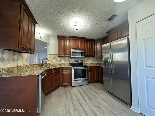 a kitchen with stainless steel appliances granite countertop a refrigerator a sink dishwasher a stove and a refrigerator with wooden floor