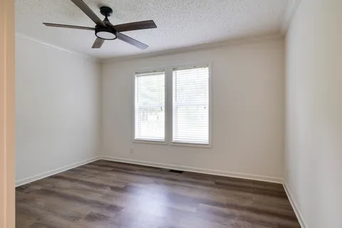 an empty room with wooden floor ceiling fan and windows