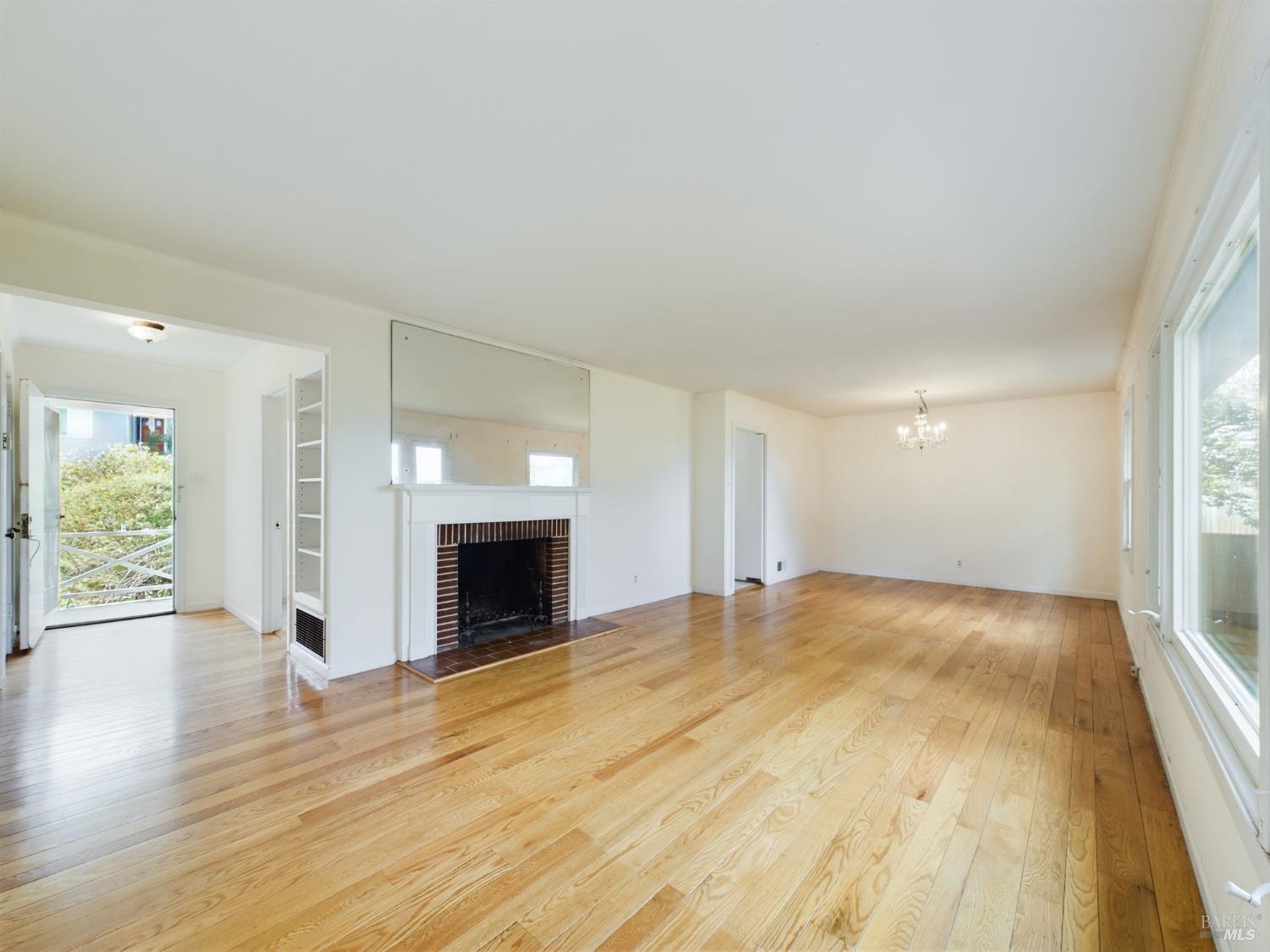 an empty room with wooden floor fireplace and windows