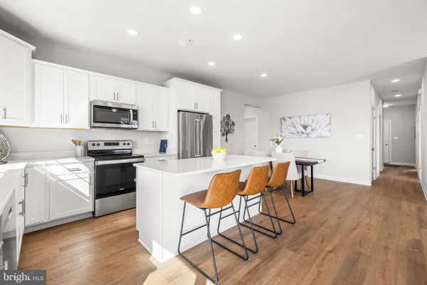 a kitchen with stainless steel appliances granite countertop a stove a sink a microwave a refrigerator white cabinets and chairs with wooden floor