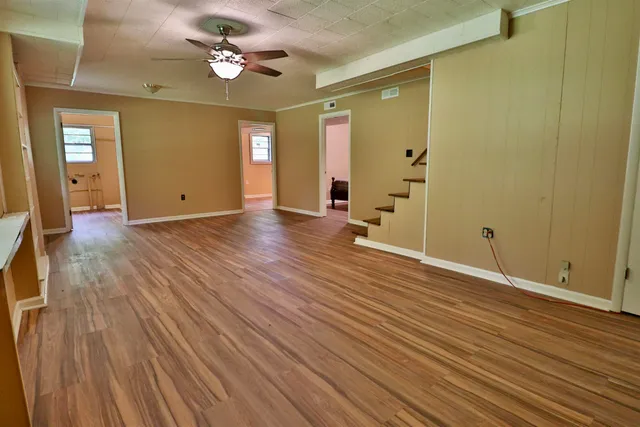a view of an empty room with wooden floor and a ceiling fan