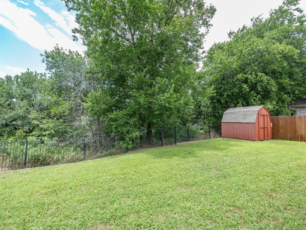 4008 Falcon Ridge Drive Haltom City, TX 76137 - Photo 38 of 40 Spacious green lawn featuring mature trees, a black metal fence, and a red gambrel roof shed with wood paneling