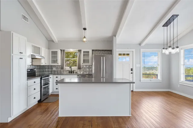 a kitchen with stainless steel appliances granite countertop a stove a sink dishwasher a refrigerator white cabinets and wooden floor next to a window