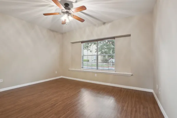 an empty room with wooden floor chandelier fan and windows