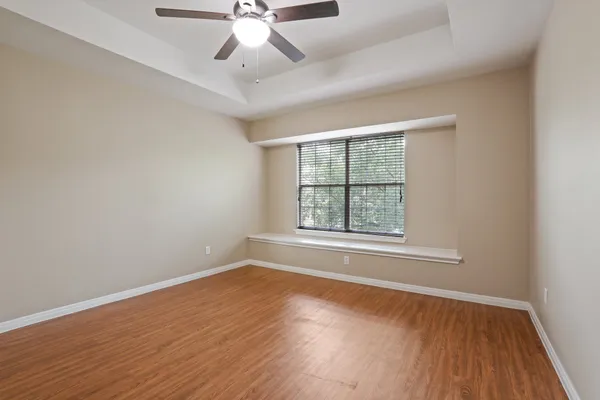 an empty room with wooden floor chandelier fan and windows