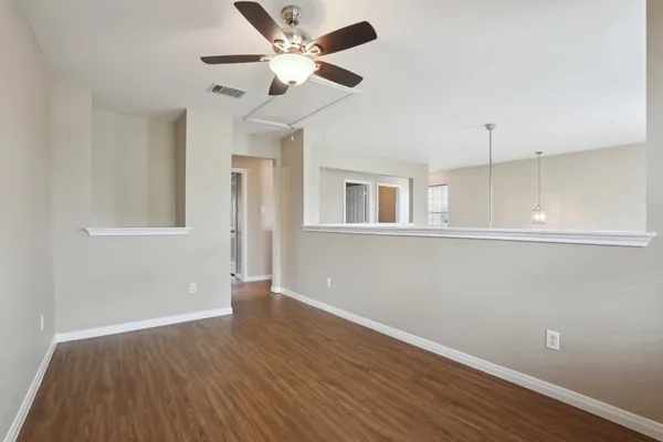 a view of an empty room with wooden floor and a ceiling fan