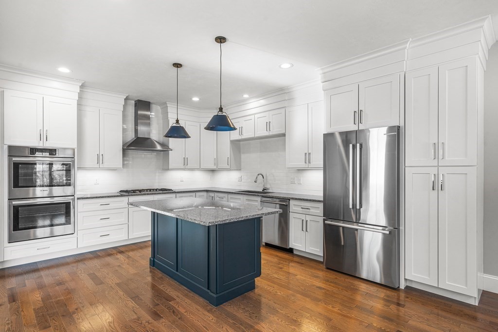 a kitchen with stainless steel appliances granite countertop a stove a refrigerator a oven and white cabinets with wooden floor