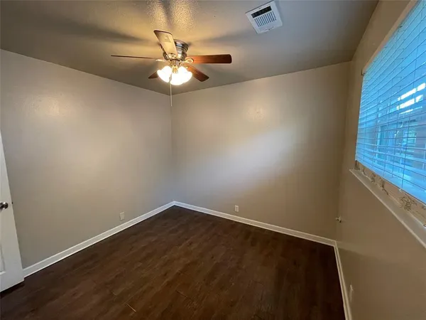 an empty room with wooden floor fan and windows