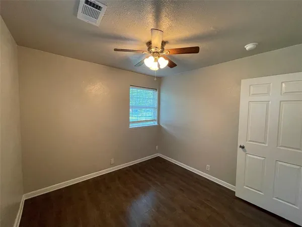 an empty room with wooden floor ceiling fan and window