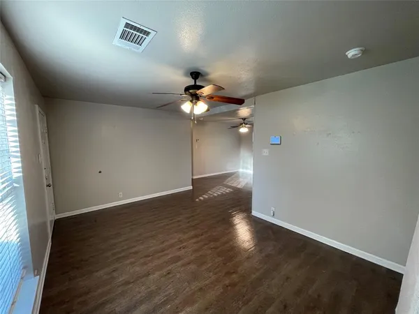 an empty room with wooden floor fan and window