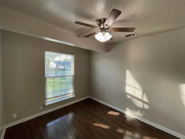 an empty room with wooden floor fan and windows
