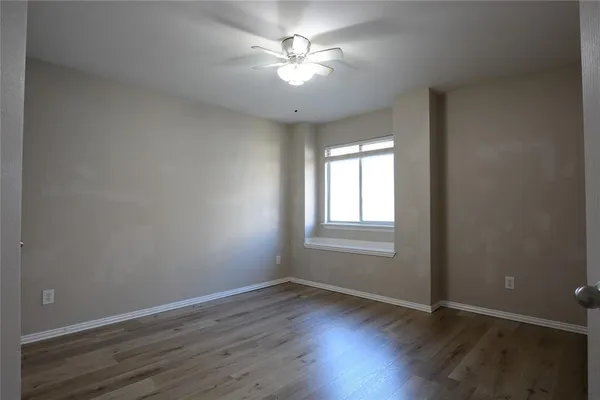 an empty room with wooden floor fan and windows
