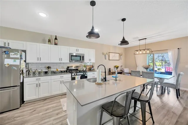 a kitchen with stainless steel appliances kitchen island granite countertop a dining table chairs stove and white cabinets