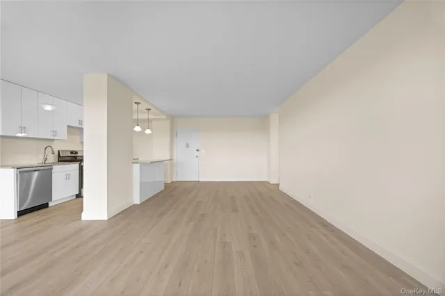 a view of empty room with wooden floor and kitchen