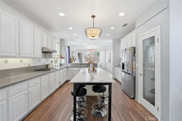 a kitchen with stainless steel appliances granite countertop a stove a refrigerator a sink dishwasher and white cabinets with wooden floor