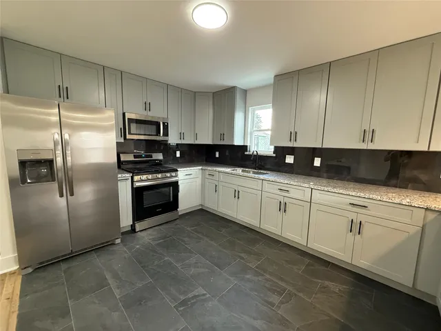 a kitchen with stainless steel appliances granite countertop a sink a stove a refrigerator a grey cabinets and a refrigerator