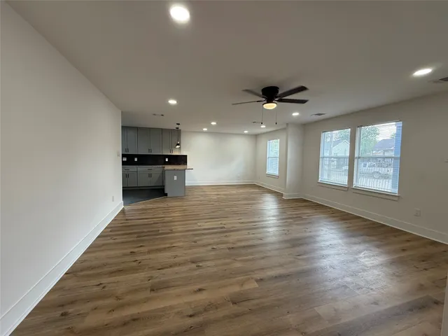 an empty room with wooden floor a ceiling fan and windows