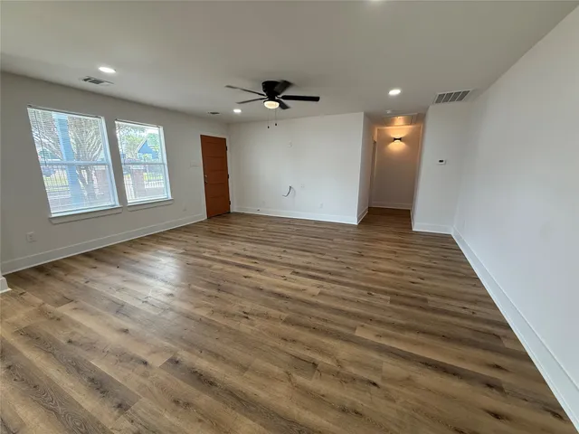 an empty room with wooden floor ceiling fan and windows