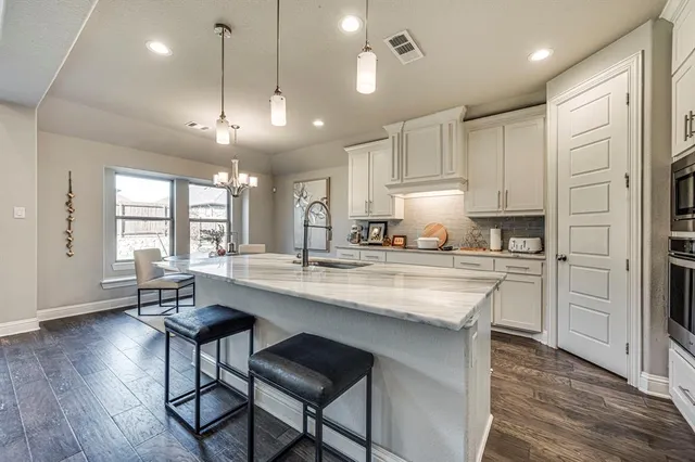 a kitchen with stainless steel appliances kitchen island granite countertop a stove a refrigerator a sink a dining table and chairs with wooden floor