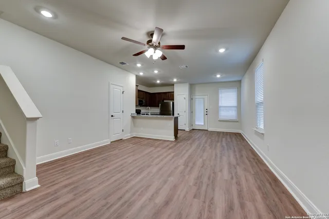 a view of an empty room with wooden floor and a kitchen