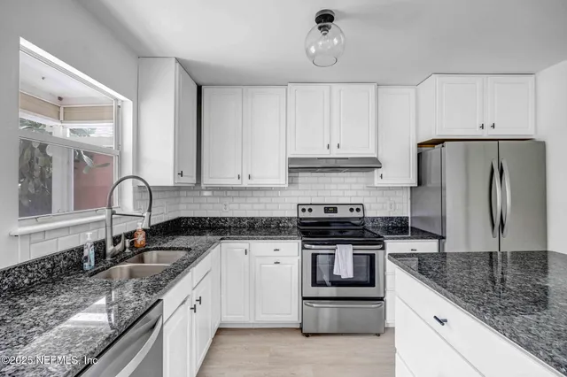 a kitchen with granite countertop a sink stainless steel appliances and white cabinets