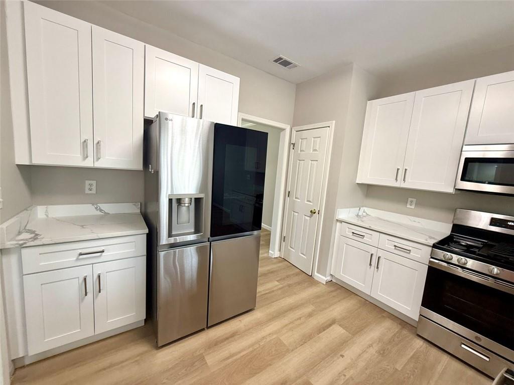 1505 Wedgefield Court Alpharetta, GA 30004 - Photo 8 of 61 a kitchen with stainless steel appliances white cabinets white and wooden floors