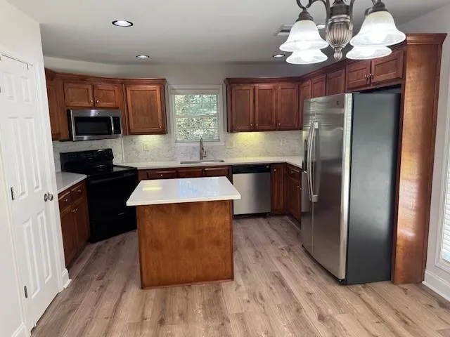 a kitchen with stainless steel appliances granite countertop a refrigerator a sink dishwasher a stove and a dining table with wooden floor