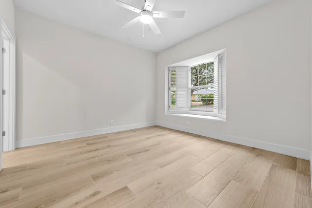 an empty room with wooden floor chandelier fan and windows