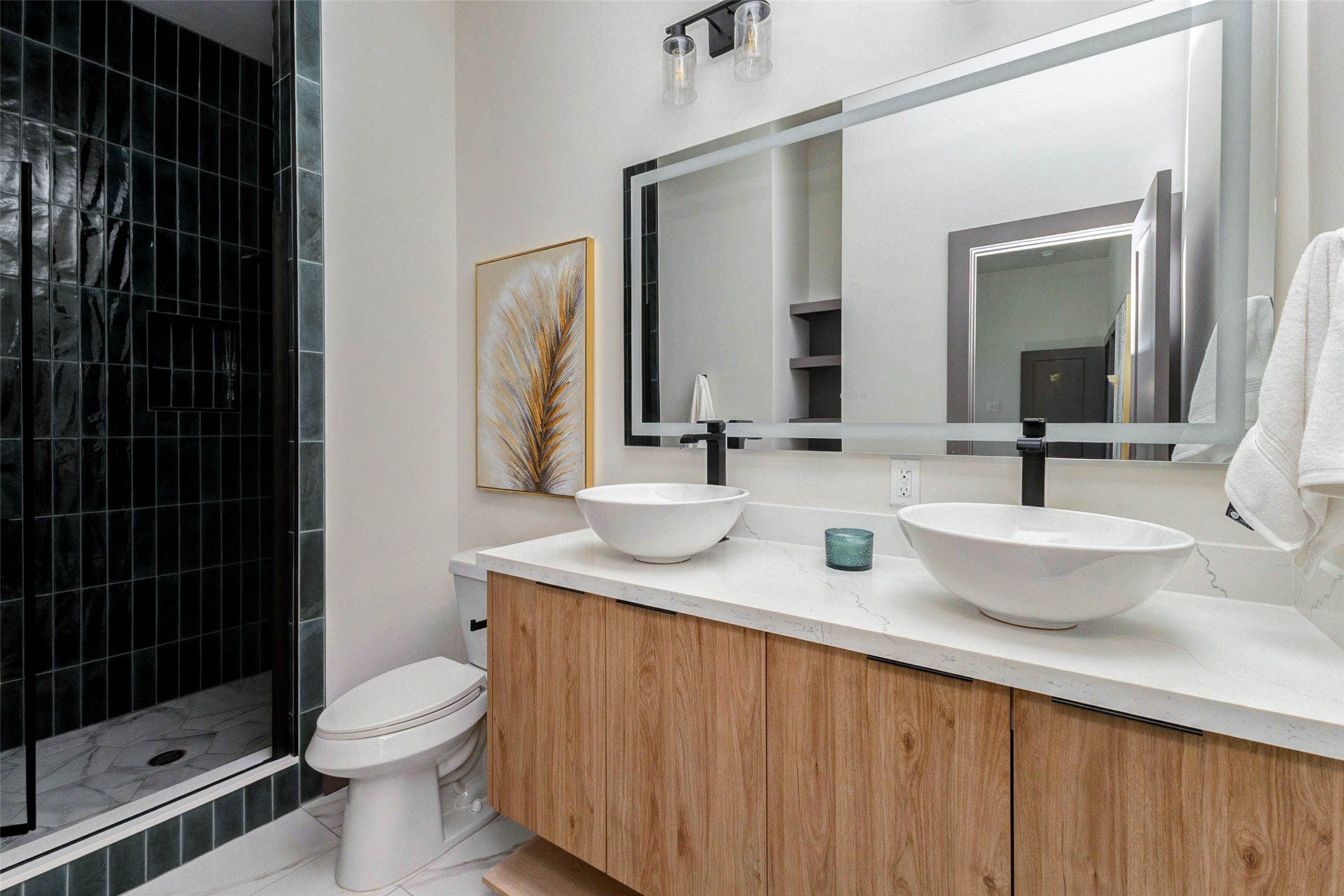 4803 Paula Street Houston, TX 77033 - Photo 16 of 28 The modern en suite bathroom features a double vanity with vessel sinks, sleek black fixtures, and a large anti-fog mirror. The wooden cabinetry adds warmth, while the neutral tones create a clean and inviting atmosphere.