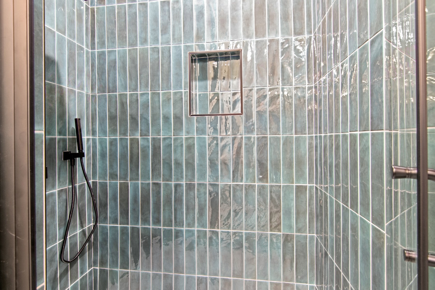 4803 Paula Street Houston, TX 77033 - Photo 17 of 28 The stylish walk-in shower with sleek blue-green glass floor to ceiling tiles features a built-in niche for convenient storage.