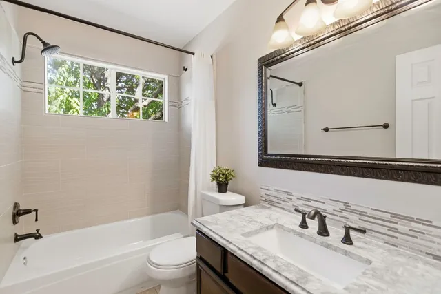 a bathroom with a granite countertop sink a toilet a large mirror and shower