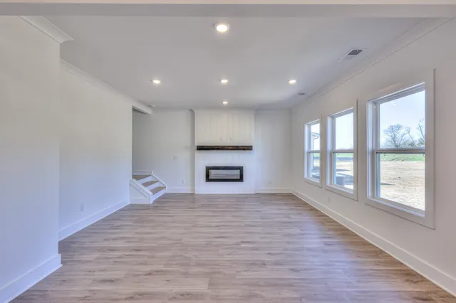 a view of an empty room with wooden floor kitchen view and a window