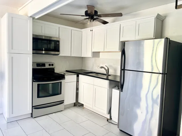 a kitchen with stainless steel appliances granite countertop a refrigerator a microwave a sink and white cabinets