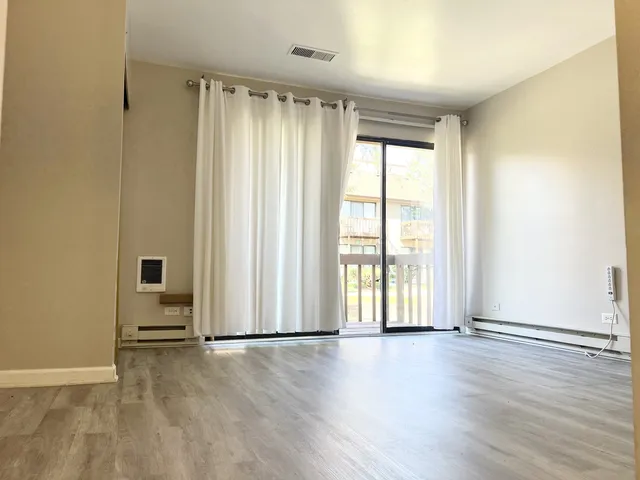 an empty room with wooden floor and windows with curtains