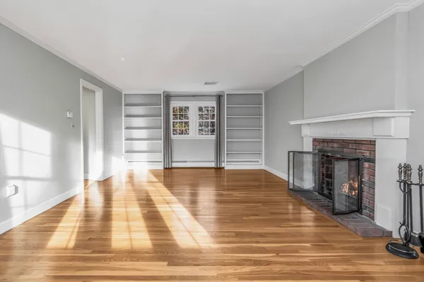 a view of an empty room with wooden floor and a fireplace