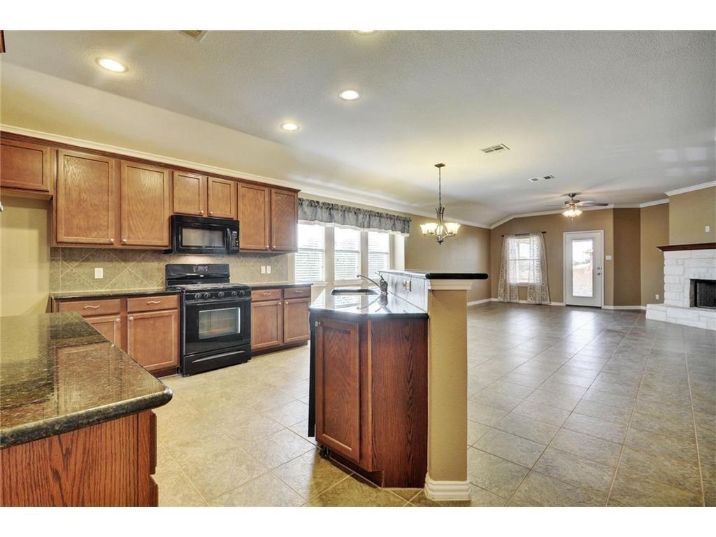2109 Granite Springs Road Leander, TX 78641 - Photo 7 of 30 An open concept kitchen features warm wood cabinetry, gleaming stone countertops, and integrated appliances.