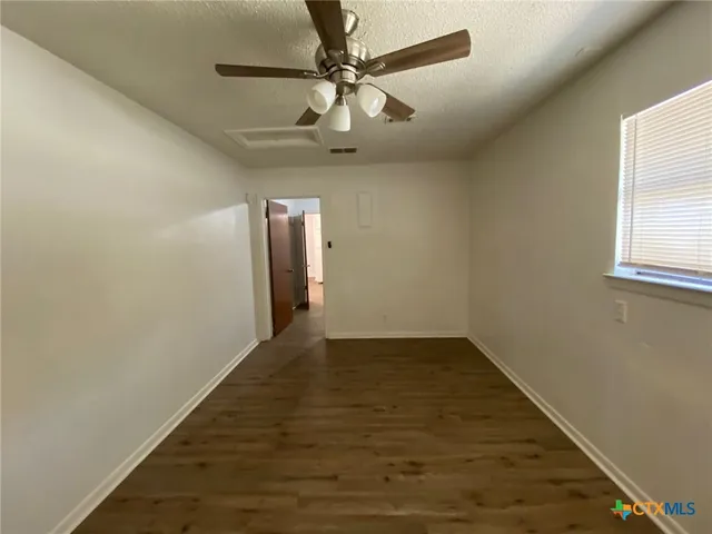 an empty room with wooden floor chandelier fan and windows