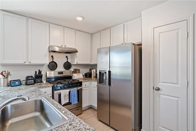 a kitchen with stainless steel appliances granite countertop a refrigerator a stove and a sink with wooden floor