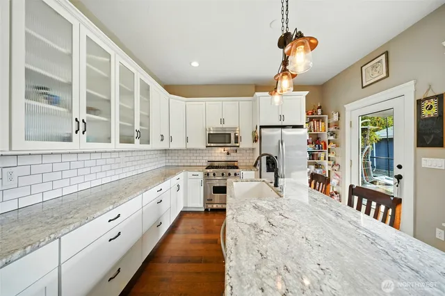 a kitchen with stainless steel appliances kitchen island granite countertop a refrigerator oven a sink dishwasher and white cabinets with wooden floor
