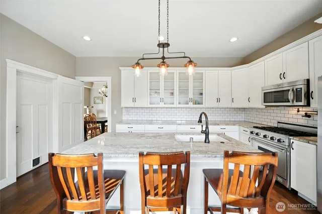 a kitchen with stainless steel appliances granite countertop a stove top oven a sink a dining table and chairs