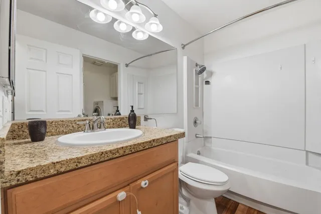 a bathroom with a granite countertop sink a toilet a mirror a bathtub and shower
