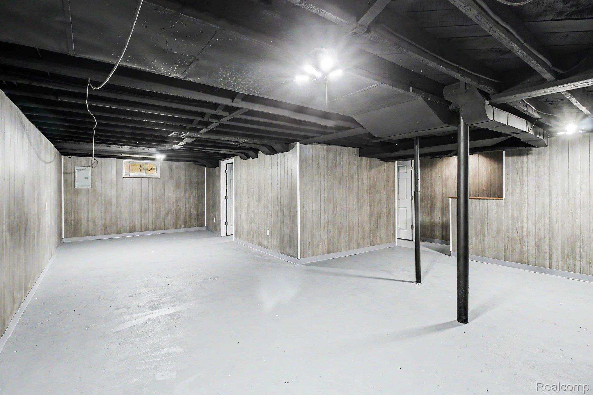 207 Elms Road Flushing, MI 48433 - Photo 22 of 30 Expansive open basement area featuring painted concrete flooring, paneled walls, exposed ceiling joists, and multiple lighting fixtures