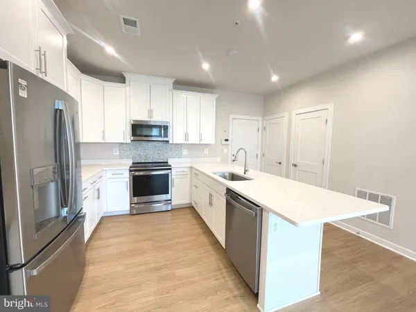 a large kitchen with a large counter top a sink stainless steel appliances and cabinets