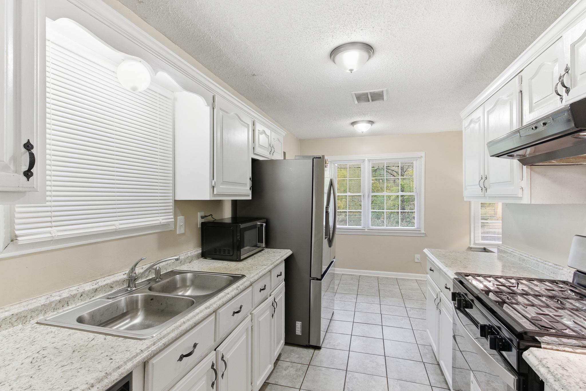 5002 Benjestown Road Memphis, TN 38127 - Photo 8 of 29 Kitchen featuring stainless steel range with gas cooktop, white cabinets, black microwave, light tile patterned floors, and a textured ceiling