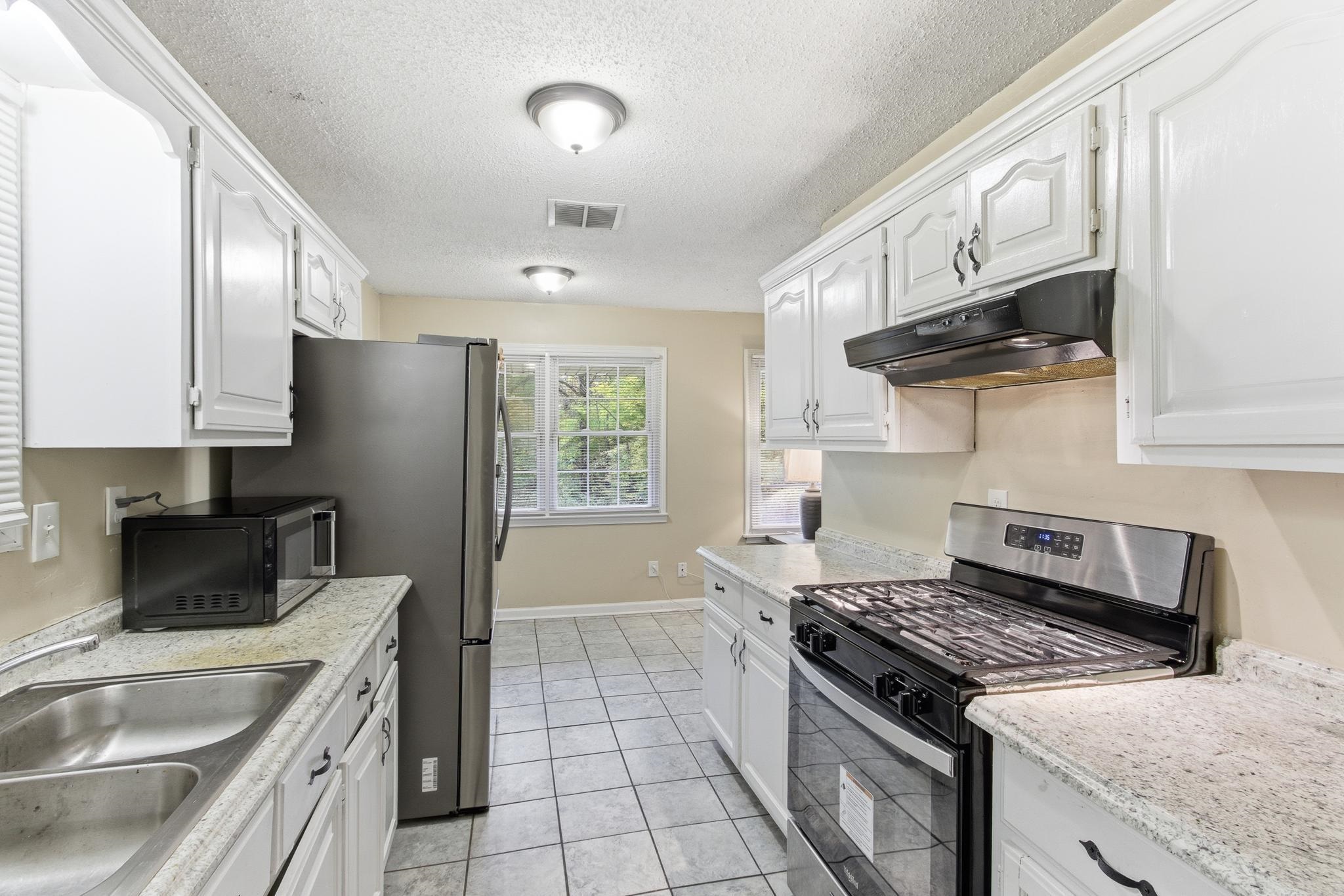 5002 Benjestown Road Memphis, TN 38127 - Photo 10 of 29 Kitchen featuring stainless steel range with gas stovetop, white cabinets, under cabinet range hood, black microwave, and a textured ceiling
