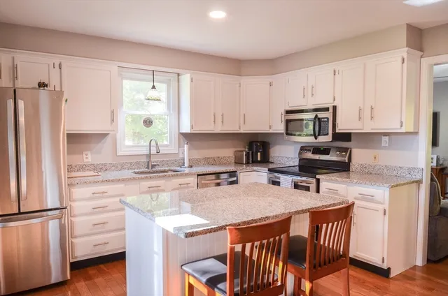 a kitchen with stainless steel appliances granite countertop a stove a sink a microwave a refrigerator and white cabinets