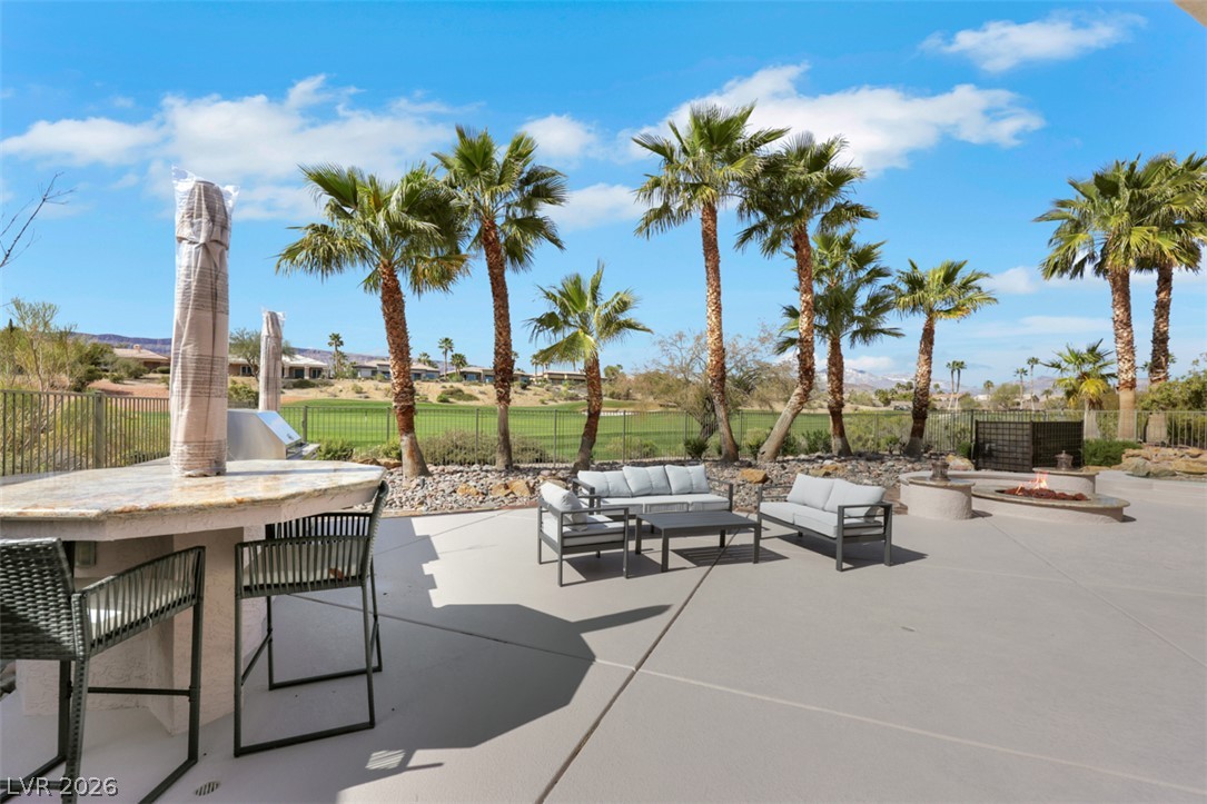5015 Rivedro Street Las Vegas, NV 89135 - Photo 64 of 91 An inviting concrete patio overlooks a verdant golf course, featuring an outdoor kitchen, bar seating, and a fire pit.