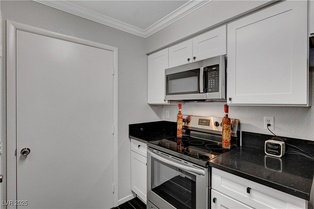8101 West Flamingo Road, Unit 1163 Las Vegas, NV 89147 - Photo 11 of 45 Kitchen with appliances with stainless steel finishes, ornamental molding, a textured wall, white cabinets, and dark stone counters